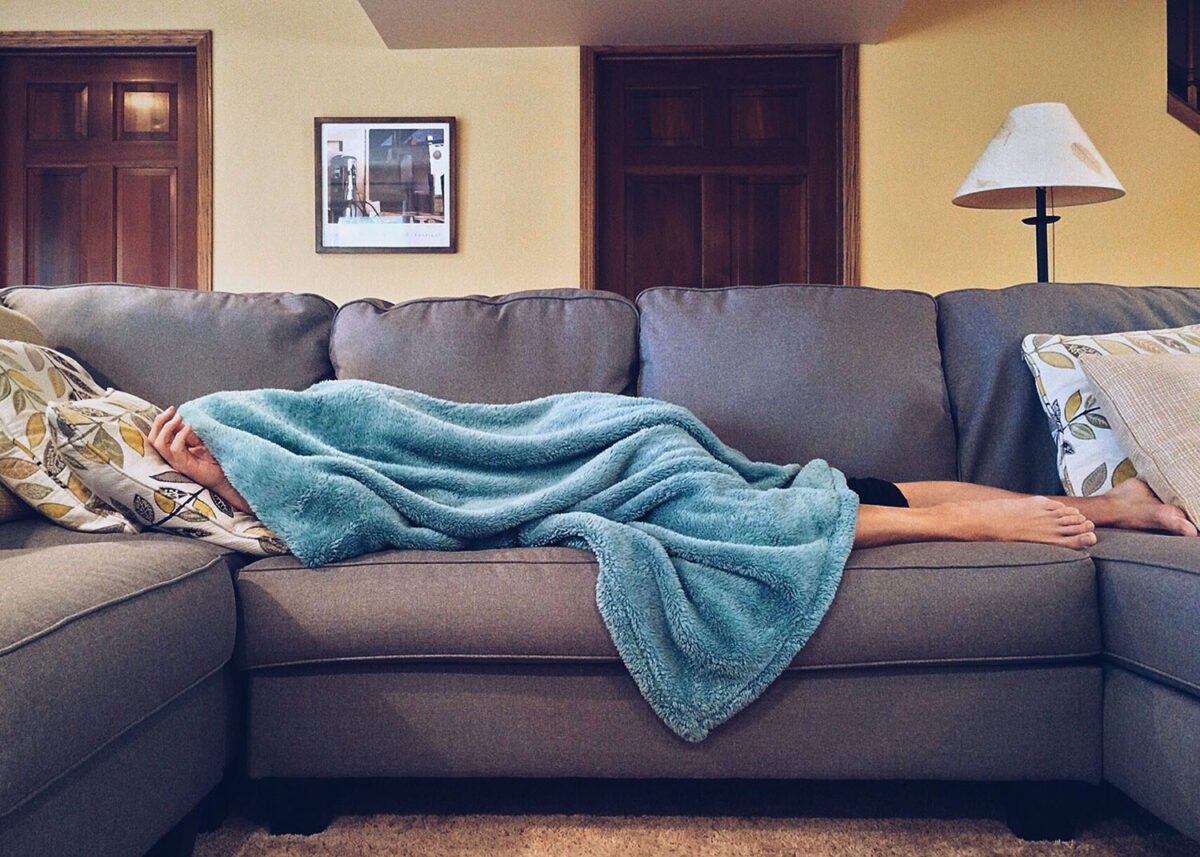 Person lying on a sofa with blue blanket depicts how to manage mental health & big city life