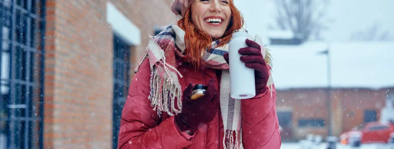 woman with a beverage bottle in her hands, smiling while it snows